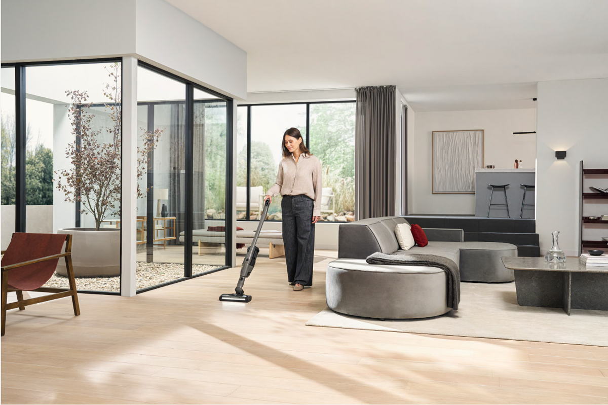 Woman using a vacuum cleaner in a modern living room with large windows.