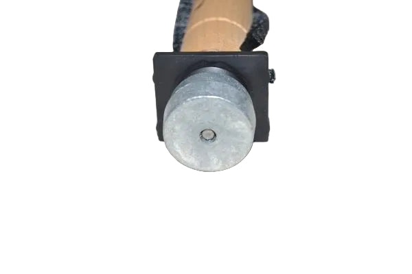 A close-up of a small cylindrical metal object with a silver circular top and a black rectangular base, attached to a tan cylindrical component on a plain light background.