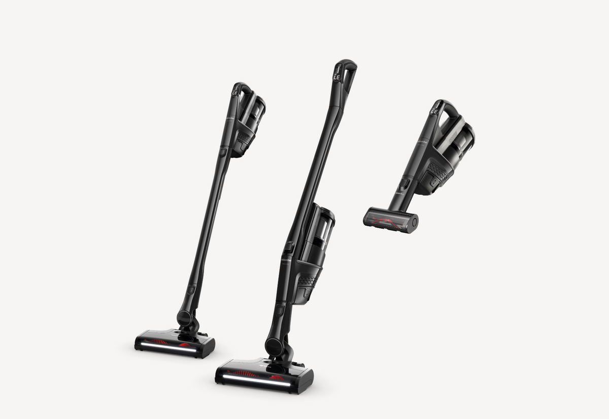 Three views of a cordless stick vacuum cleaner in black and dark gray, shown on a clean light gray background.